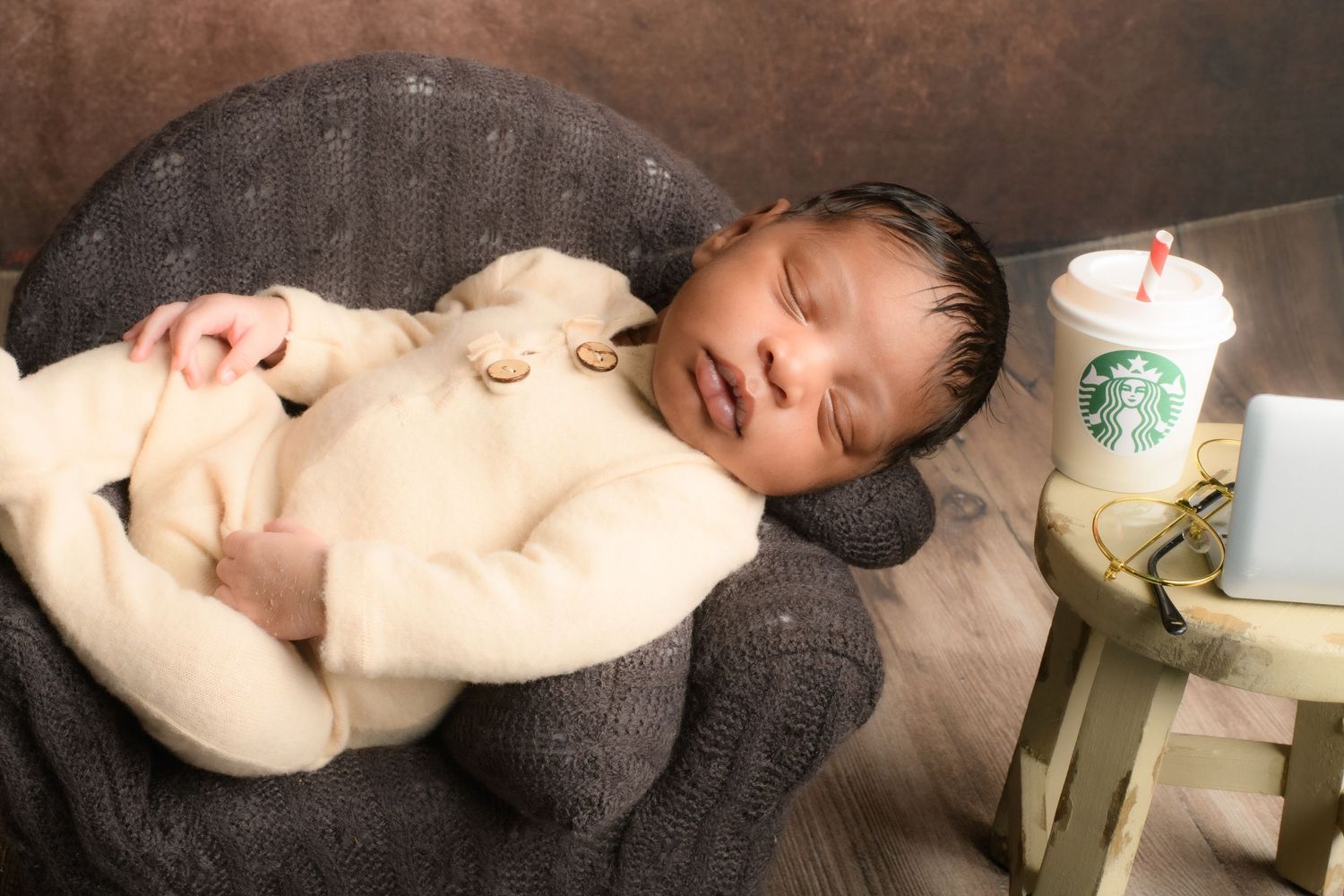 Newborn baby sleeping peacefully on dark textured blanket during professional photoshoot.