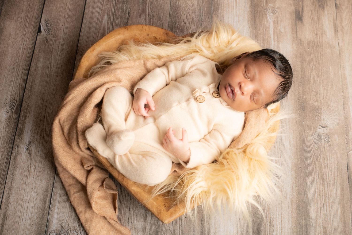 Baby resting on wooden floor with soft beige fur blanket during portrait session.