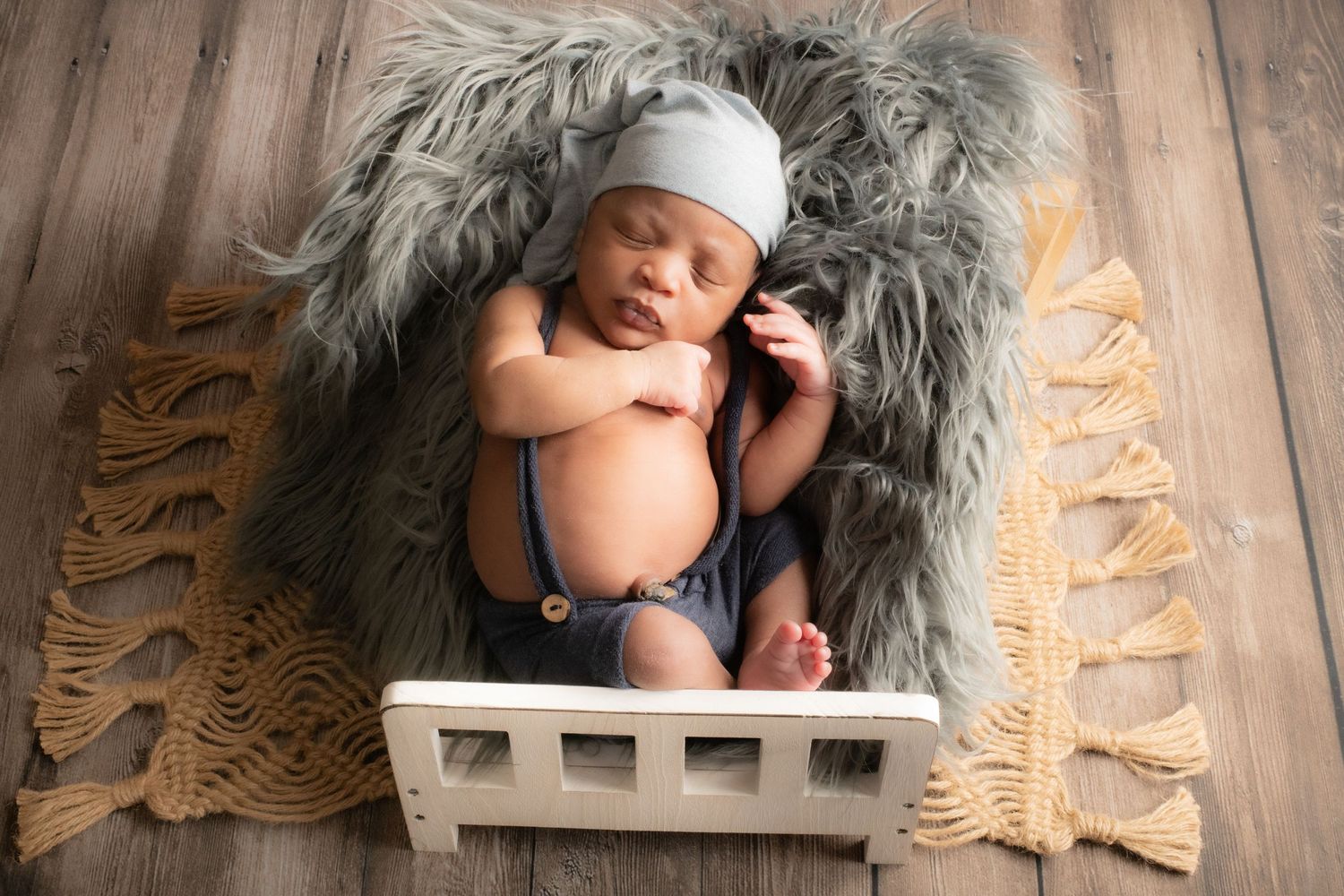 Professional newborn photography on wooden floor with grey fur backdrop.