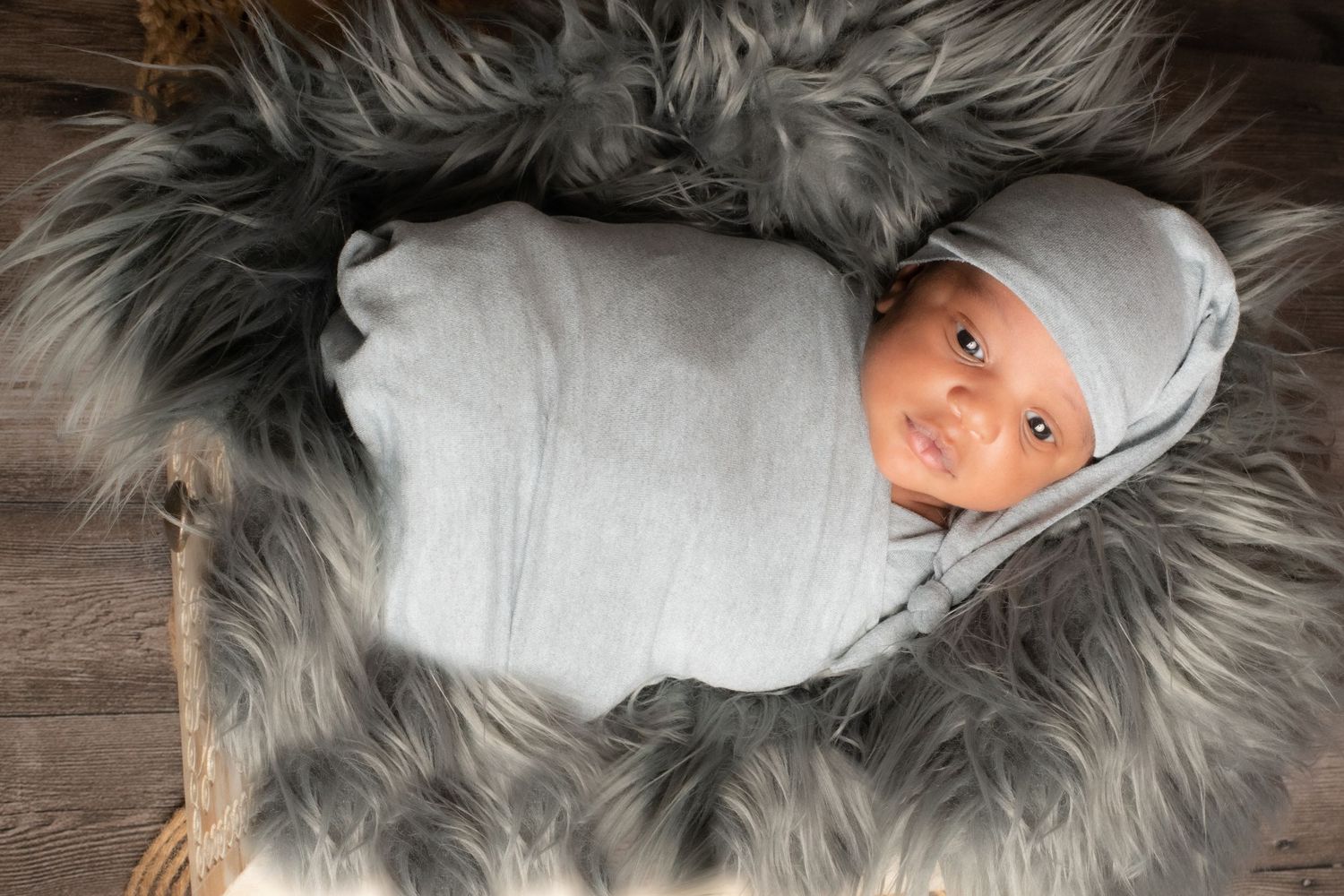 Sleeping newborn wrapped in white swaddle on grey furry rug for professional photos.