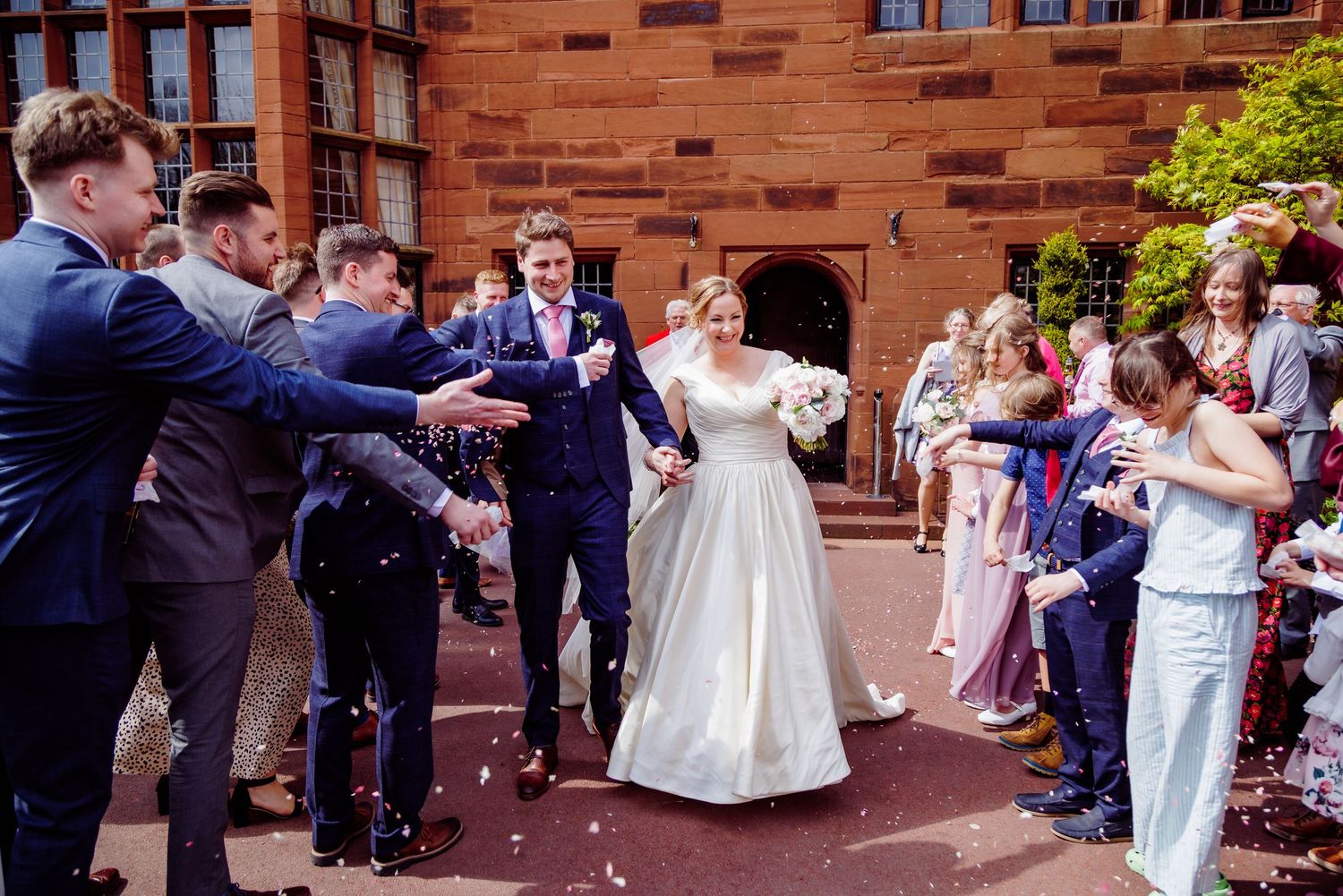 Wedding celebration outside brick building with guests throwing confetti in celebration.