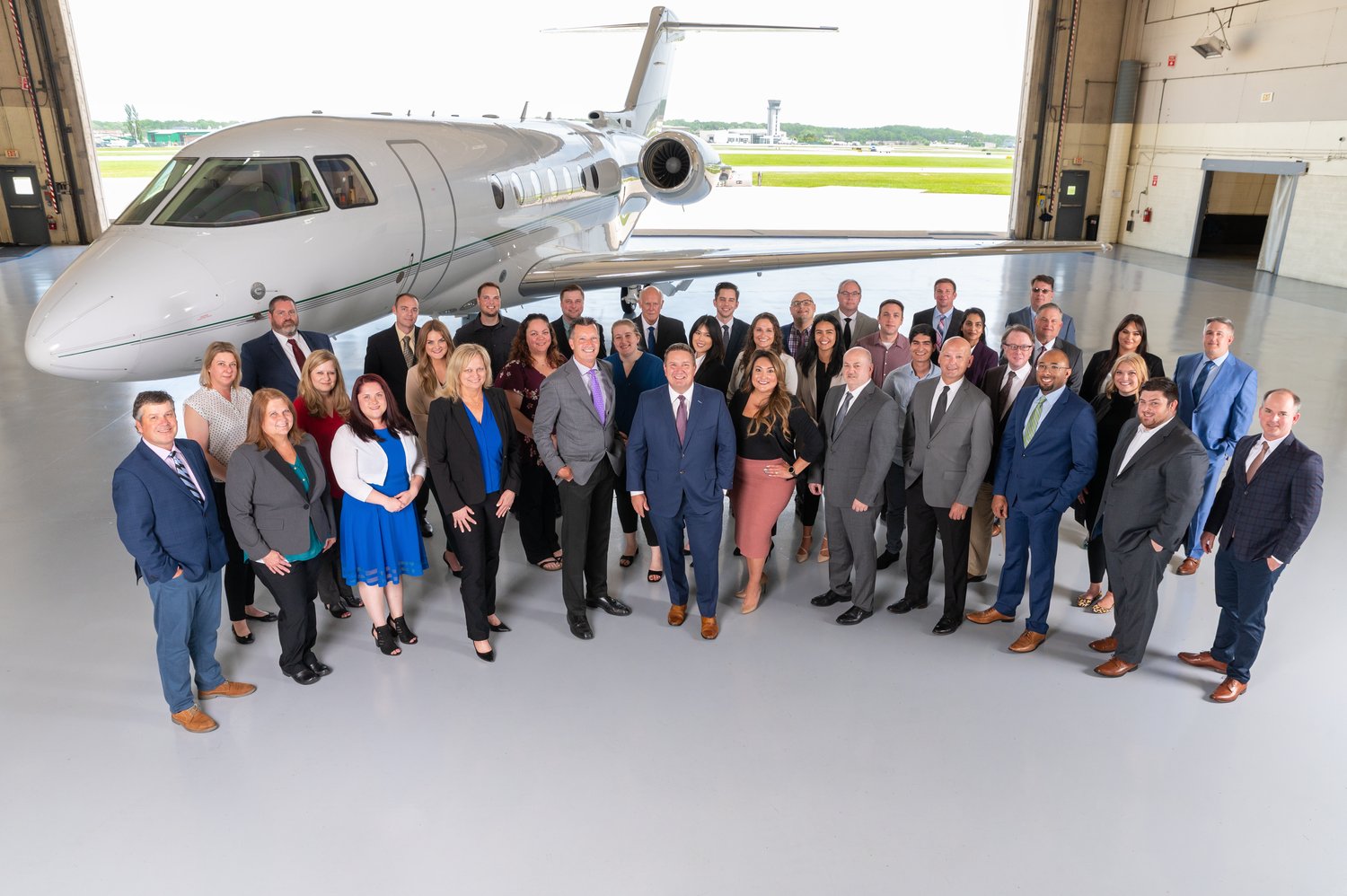 Corporate team photo of business professionals posing in front of private jet in hangar.