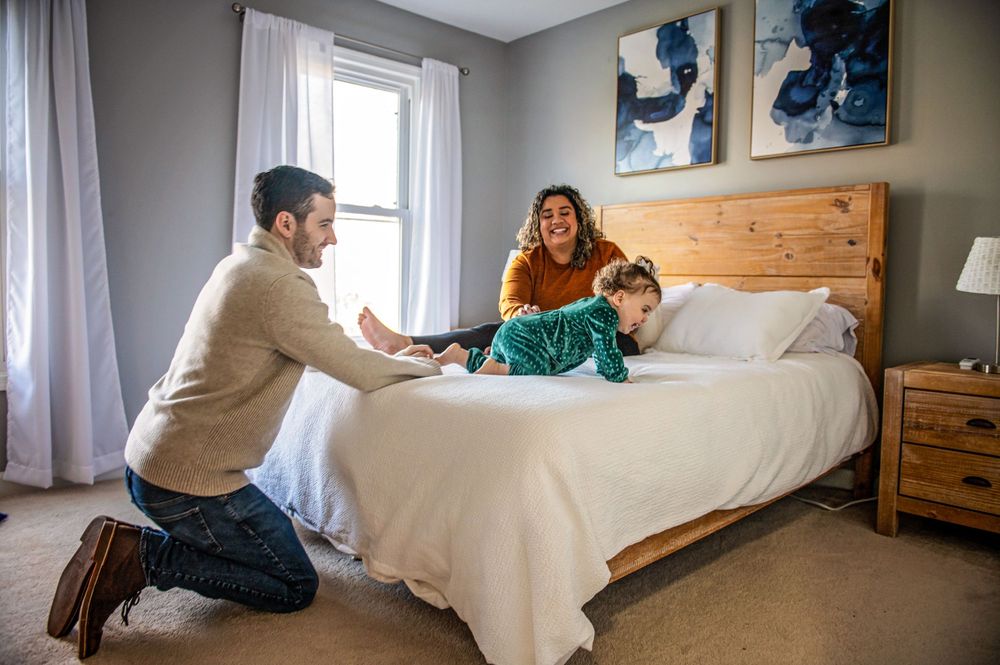 Playful family scene on white bed with wooden headboard and blue wall art.