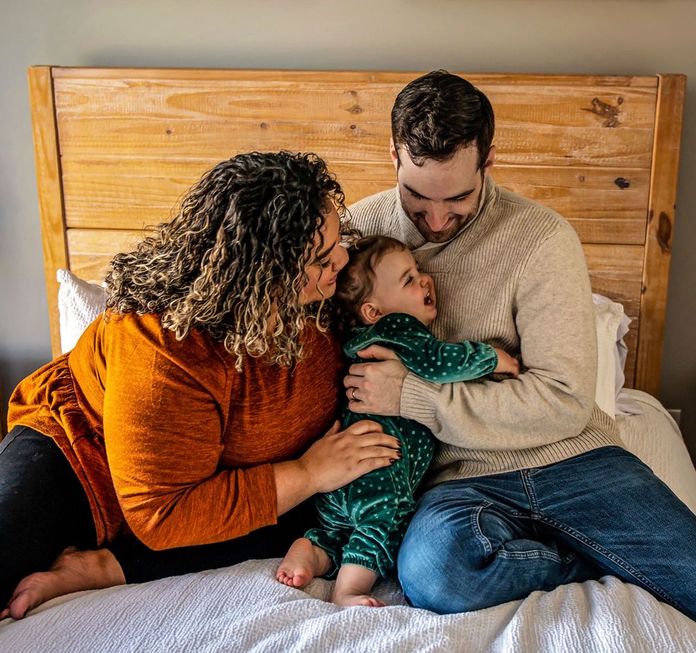 Family sharing intimate moment together while cuddling on bed with wooden headboard.