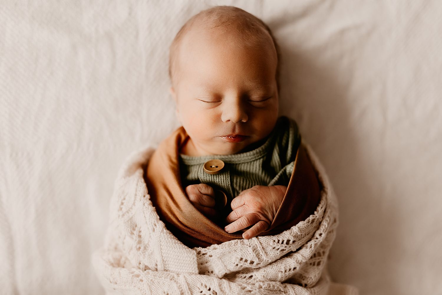 A newborn baby boy lays swaddled on the bed while sleeping during his newborn session.