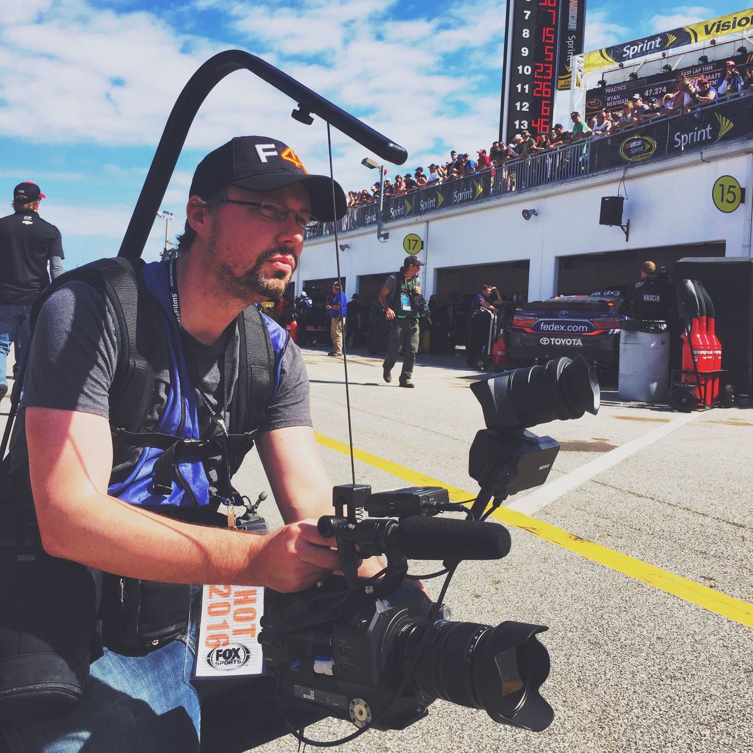 Camera operator filming with professional gear at NASCAR pit lane.