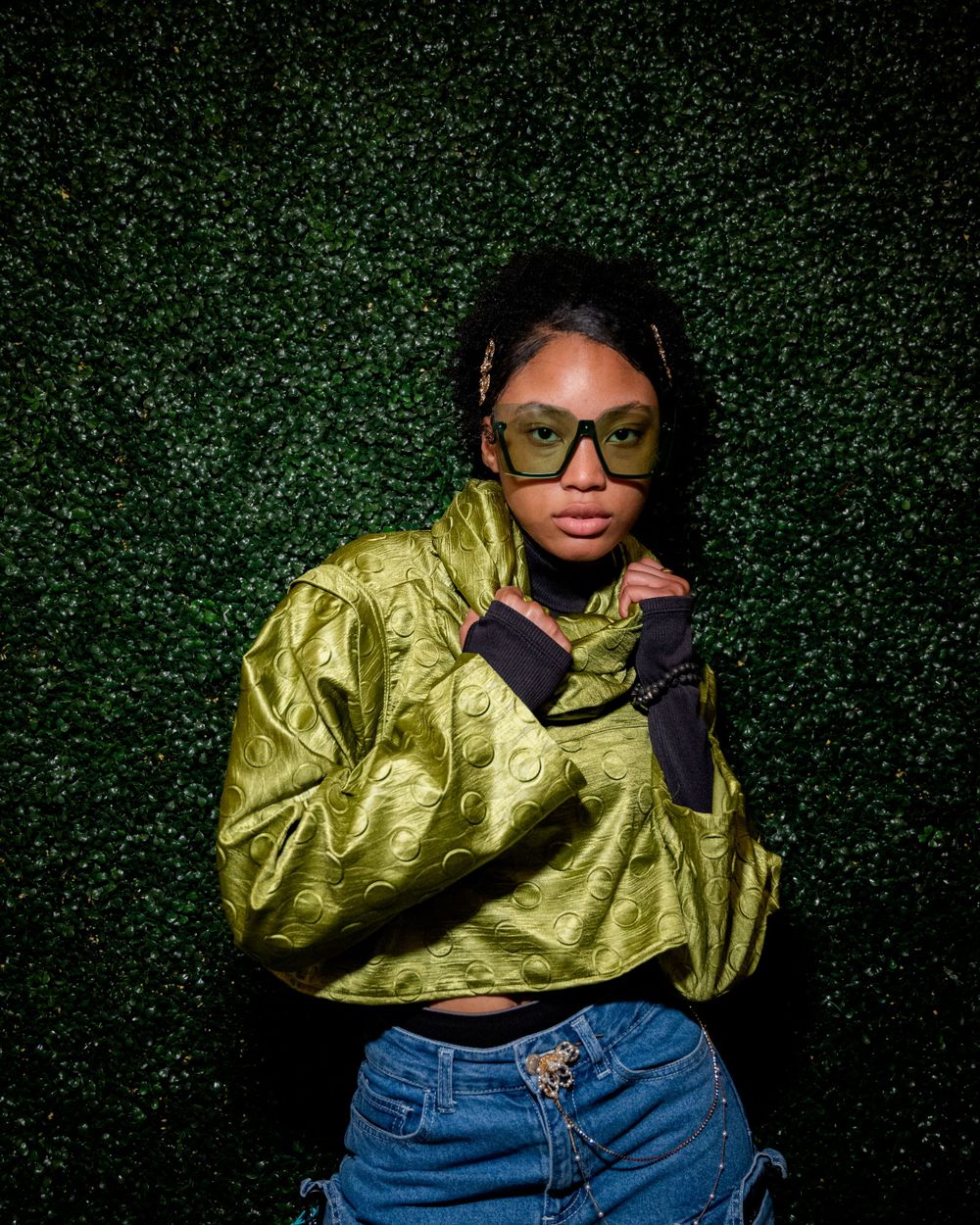 Fashion shot featuring metallic gold jacket and denim against textured green background.