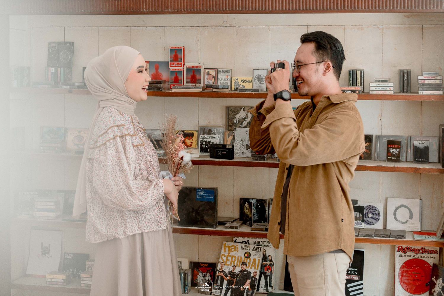 A couple laughs together while posing in front of shelves filled with vintage cameras.