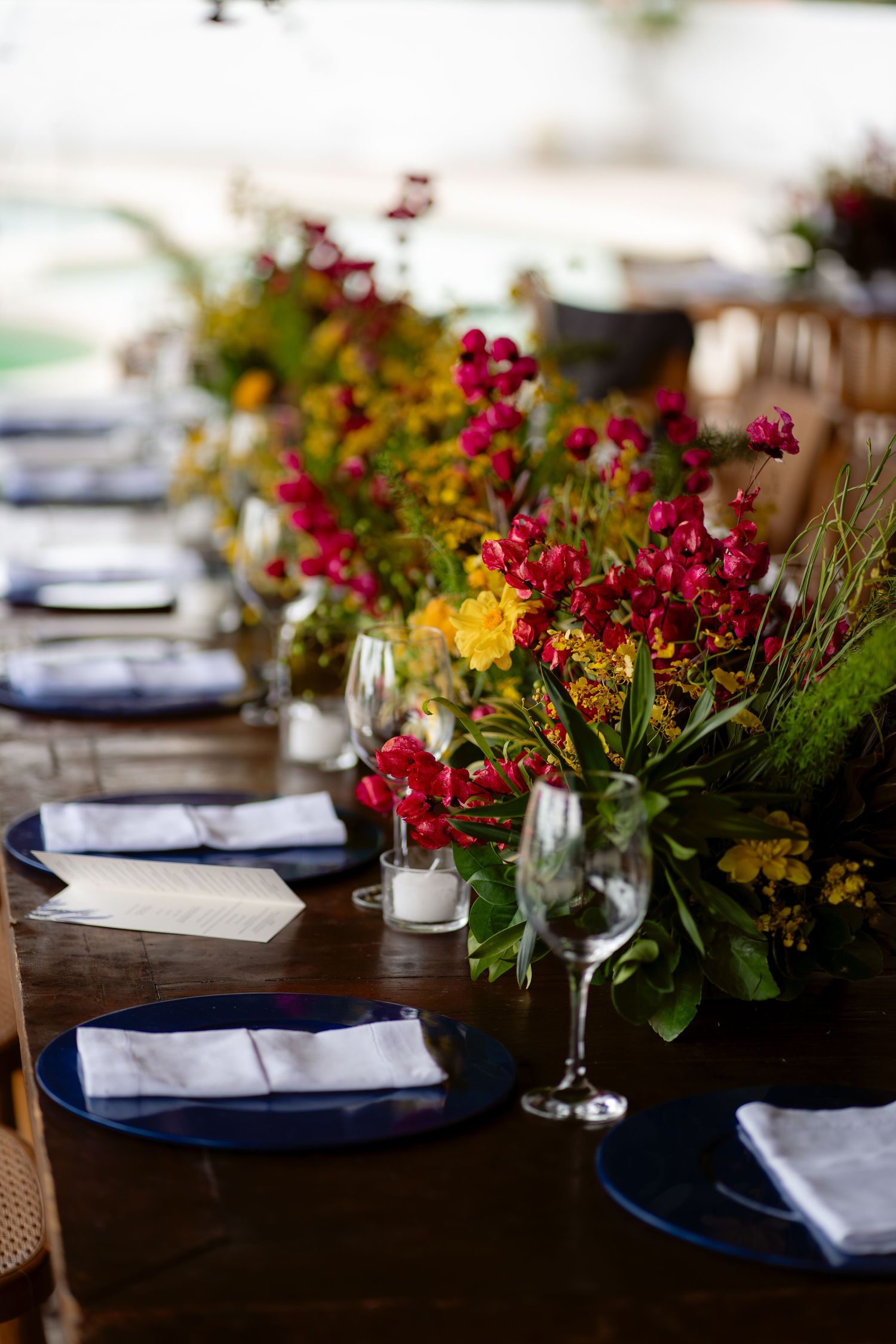 Elegant table setting with vibrant red and yellow flower arrangements and navy blue napkins.