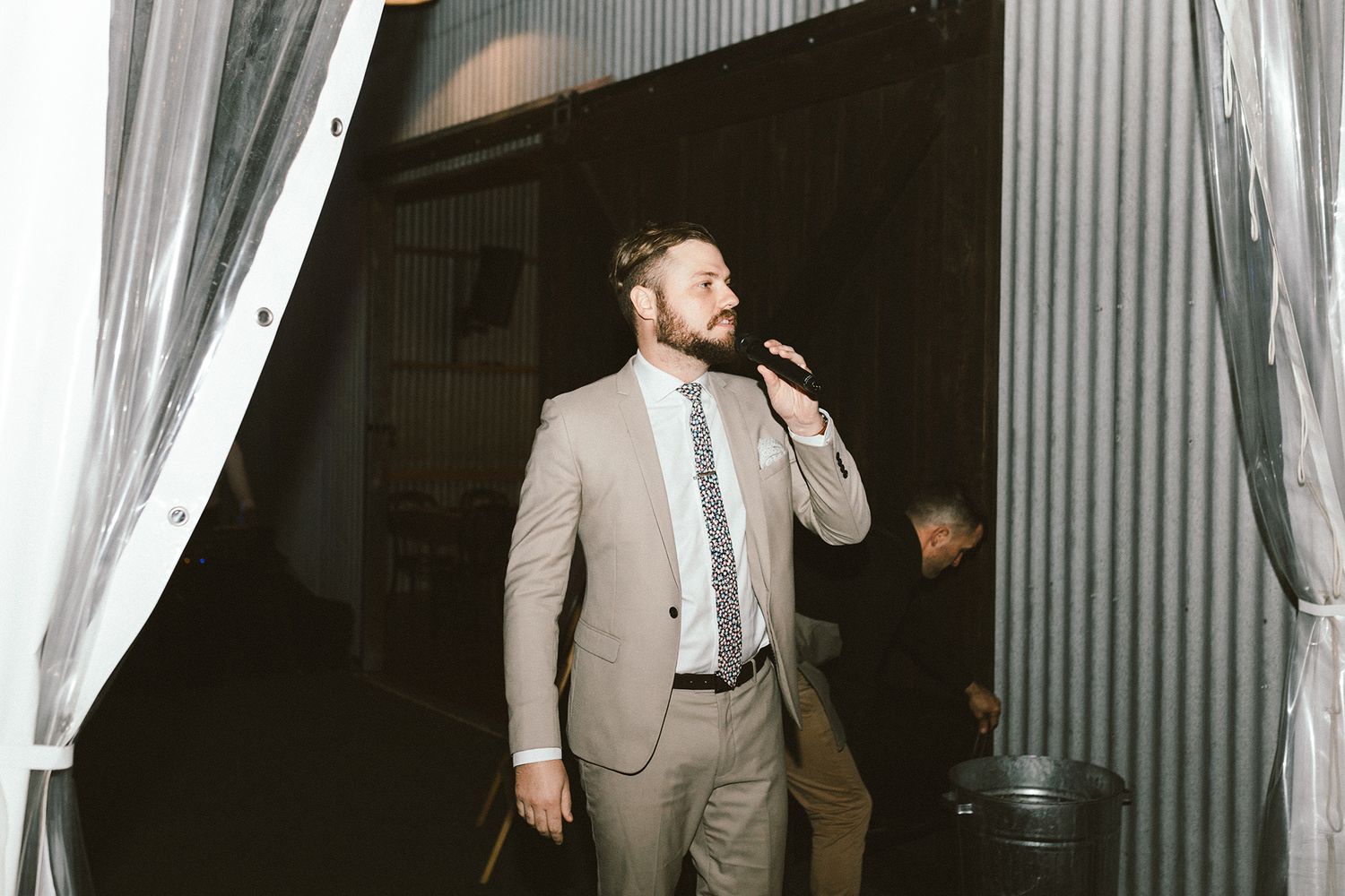 Wedding reception guests mingling in an industrial venue with corrugated metal walls.