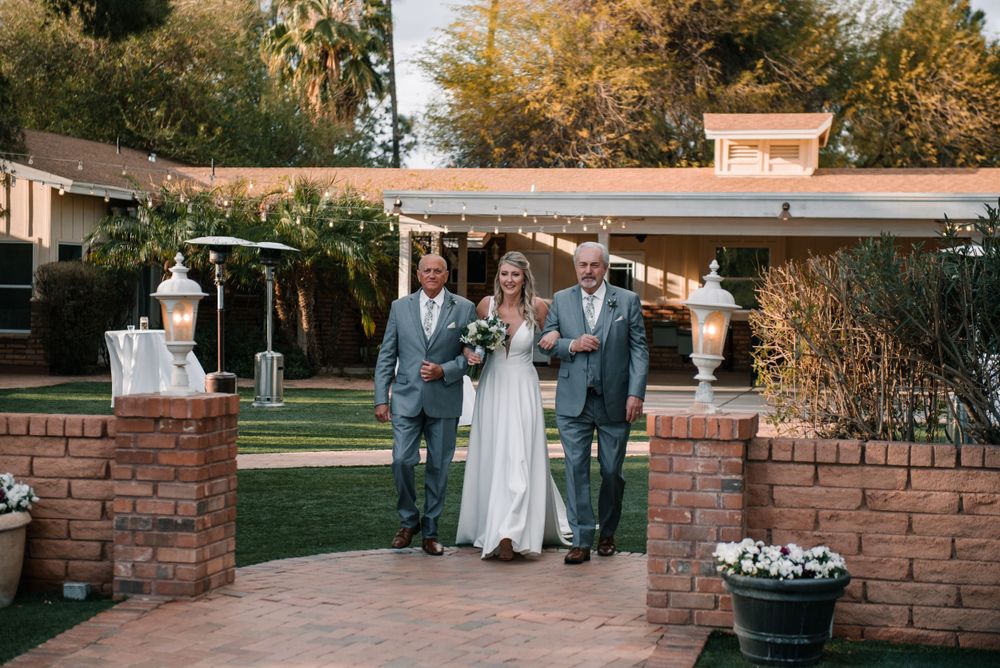 Wedding party poses between brick pillars in outdoor garden setting at dusk.