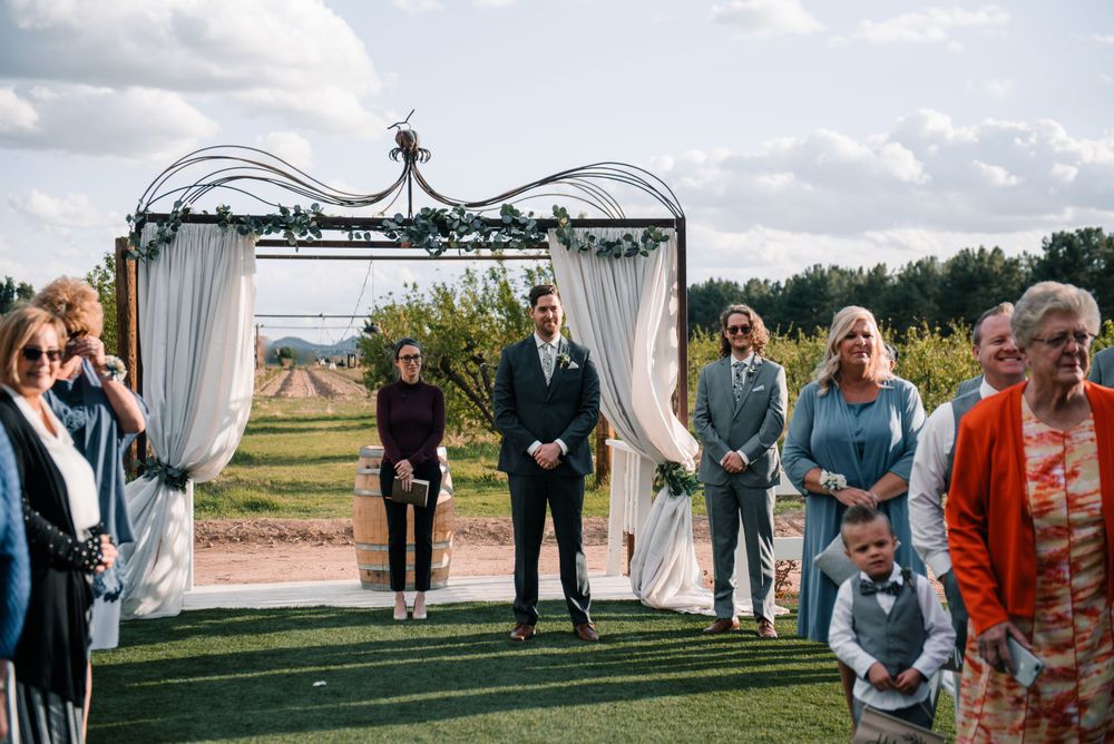 Outdoor wedding ceremony under decorated metal arch with white fabric draping and floral accents.