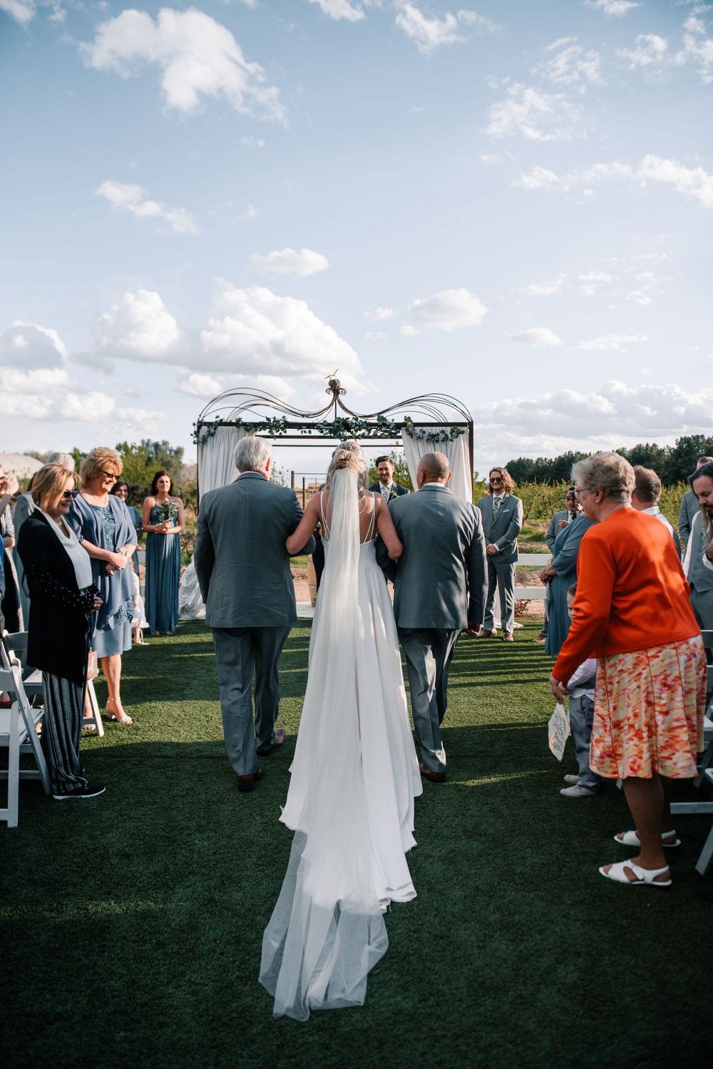 Wedding ceremony in progress under decorated arch with guests seated on lawn.