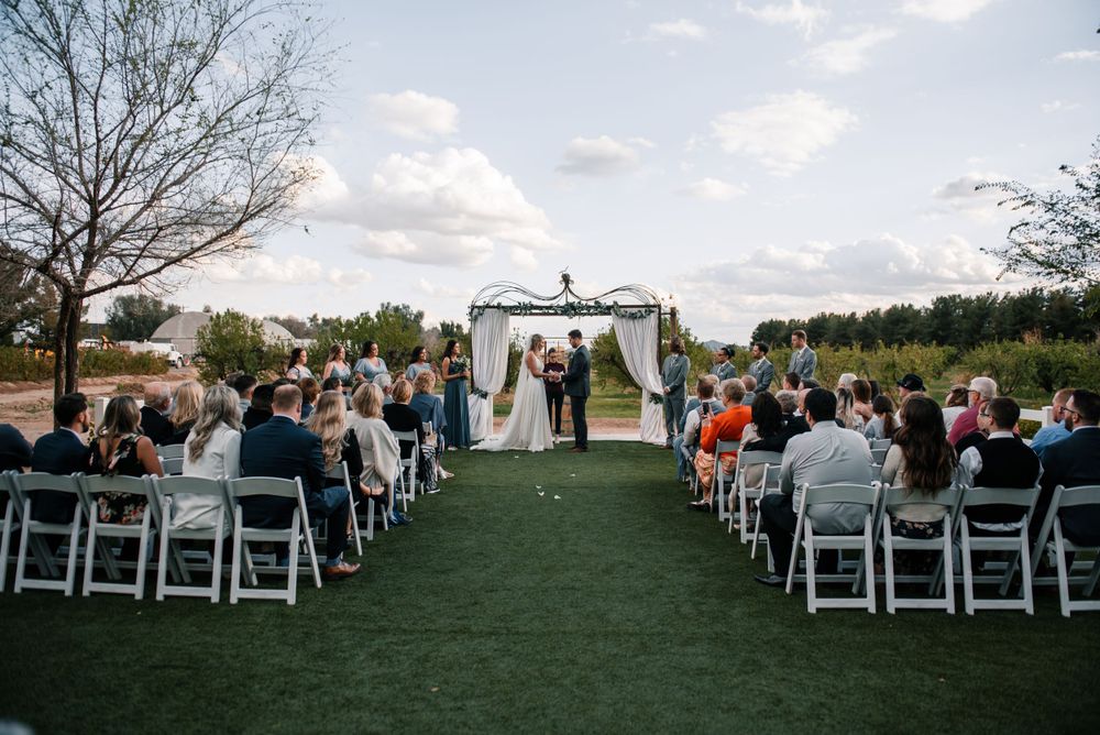 Outdoor wedding ceremony setup with white chairs and decorated arch against natural landscape.