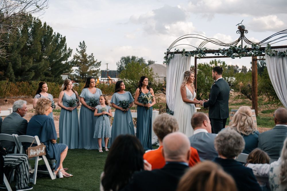 Wedding ceremony with bridesmaids in blue dresses and guests seated on white chairs.