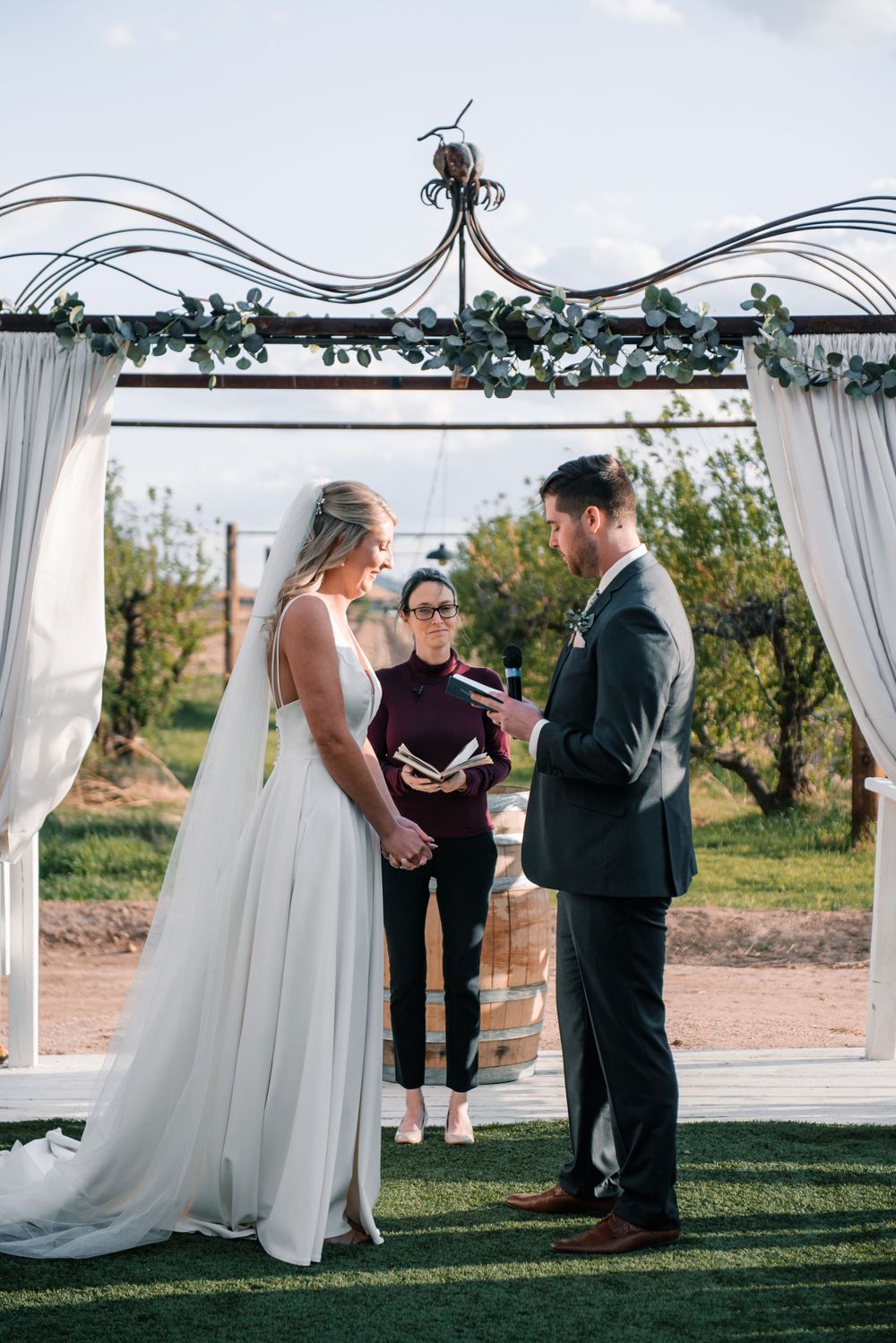 Wedding ceremony taking place under elegant white draped arch with greenery decorations.