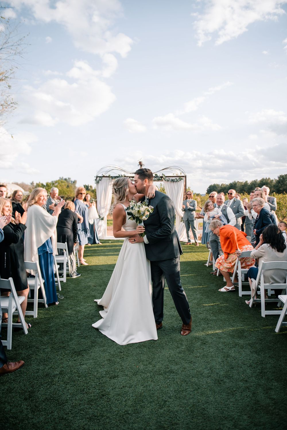 Wedding couple shares first dance surrounded by guests on outdoor lawn.