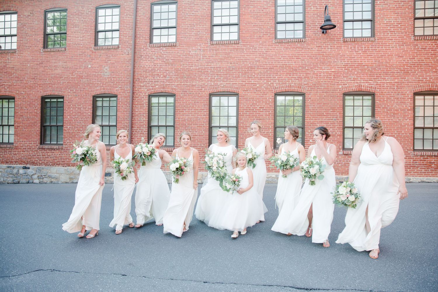 Wedding party in white dresses walking together against a brick building exterior.