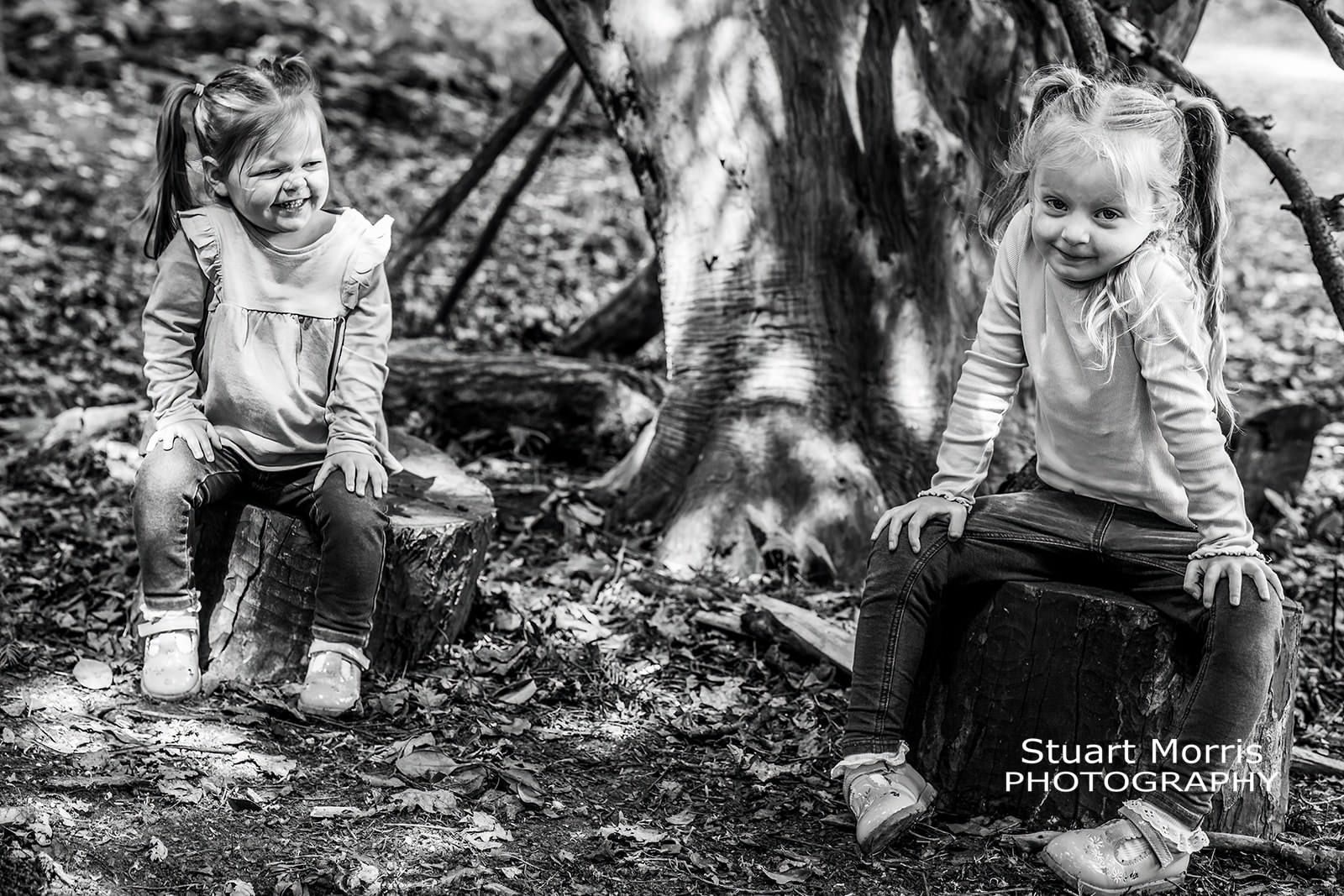 2 young girls sit on tree trunks in the woods at Walton hall. mini portrait photo session by Stuart Morris Photography