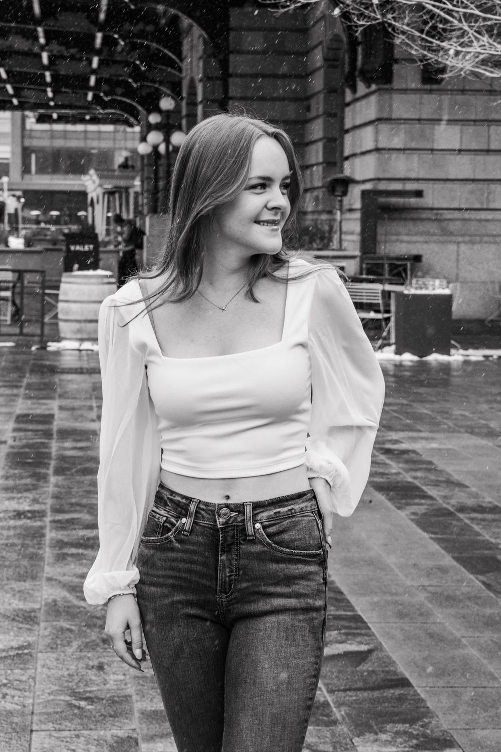 Smiling young woman in white top and jeans walking in black and white urban photo.