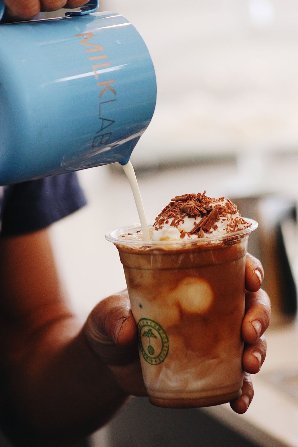 Blue pitcher pouring milk into iced coffee drinks topped with cocoa powder.