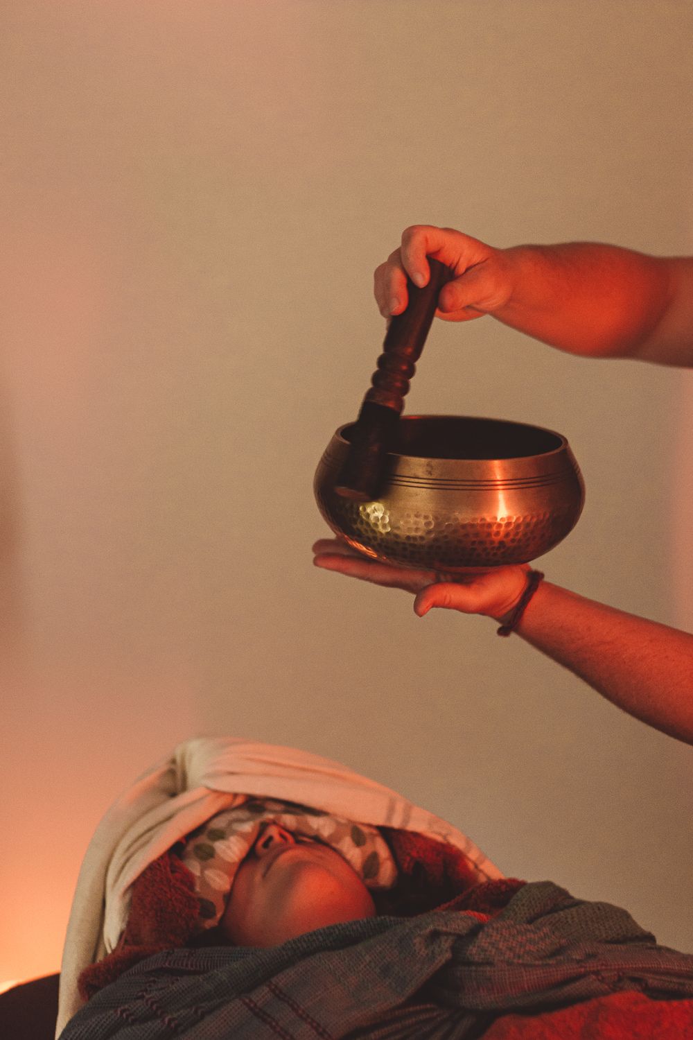 Hands holding singing bowl over person during sound healing session.