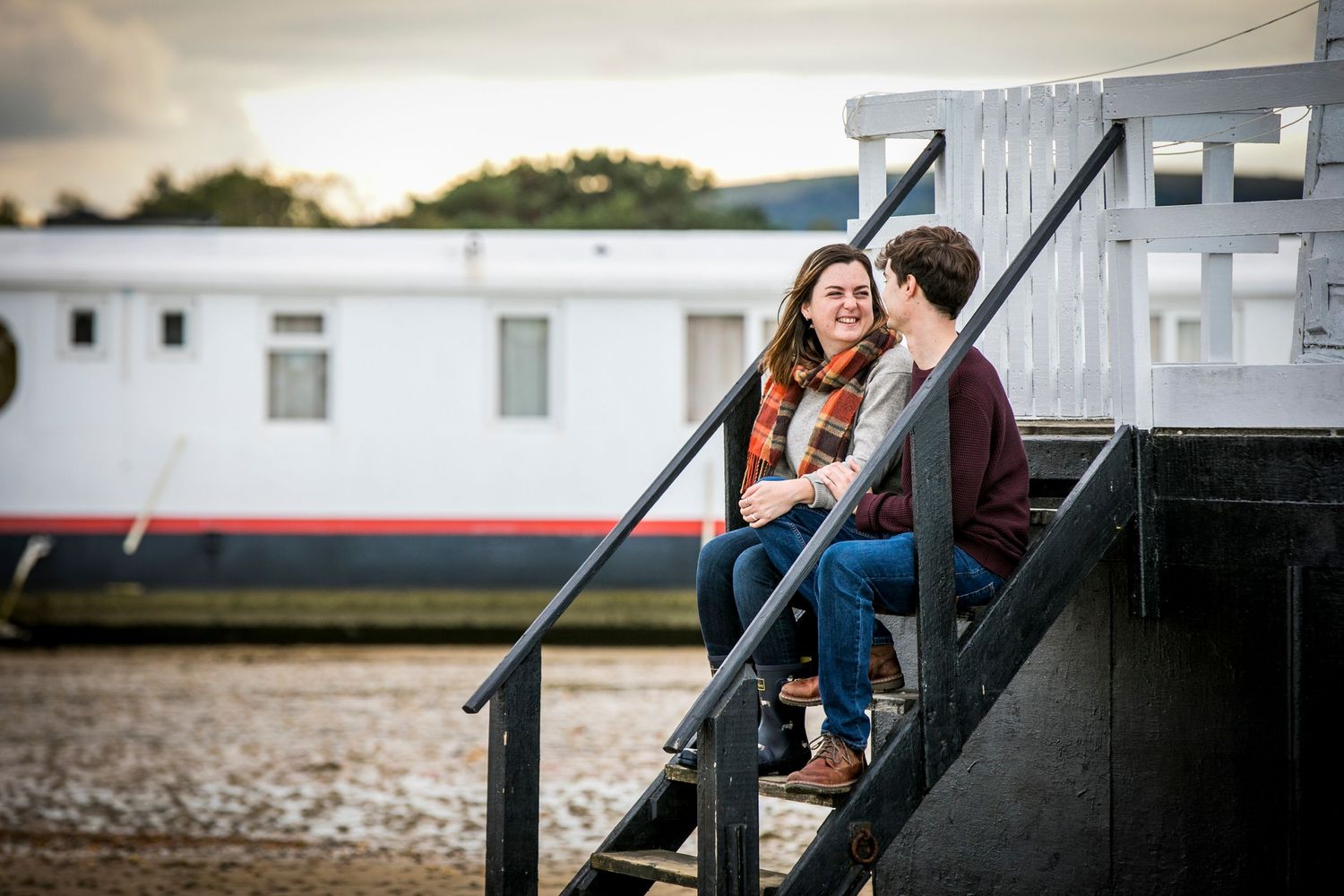 A couple shares an intimate moment on wooden stairs by the water at sunset.