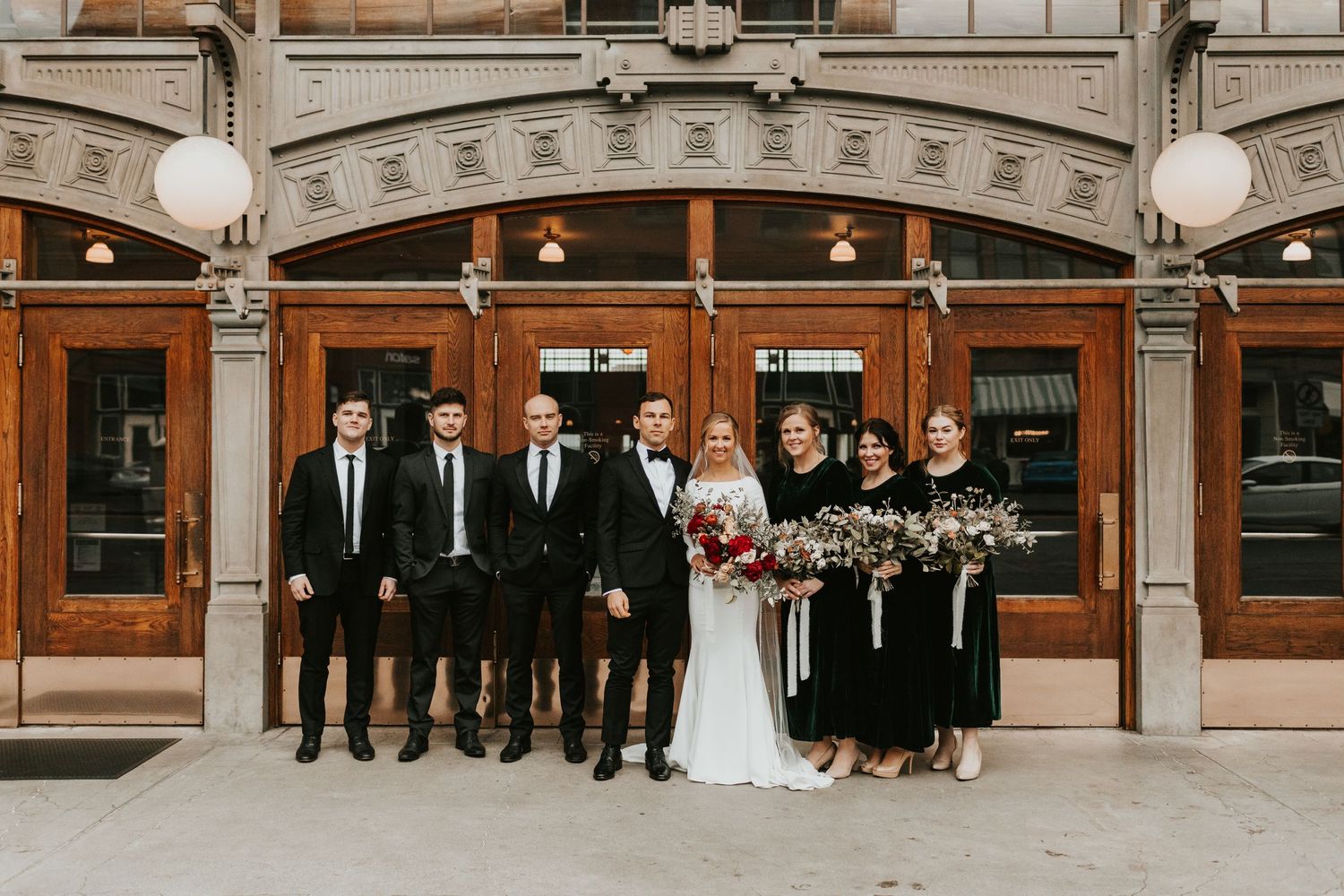 Wedding party poses in front of historic building with ornate architectural details.