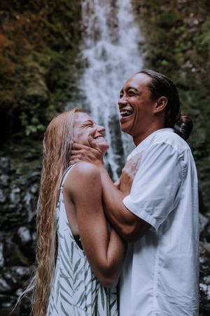 A couple laughing joyfully together in front of a waterfall.