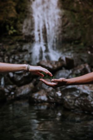 Two hands reaching towards each other in front of a cascading waterfall.