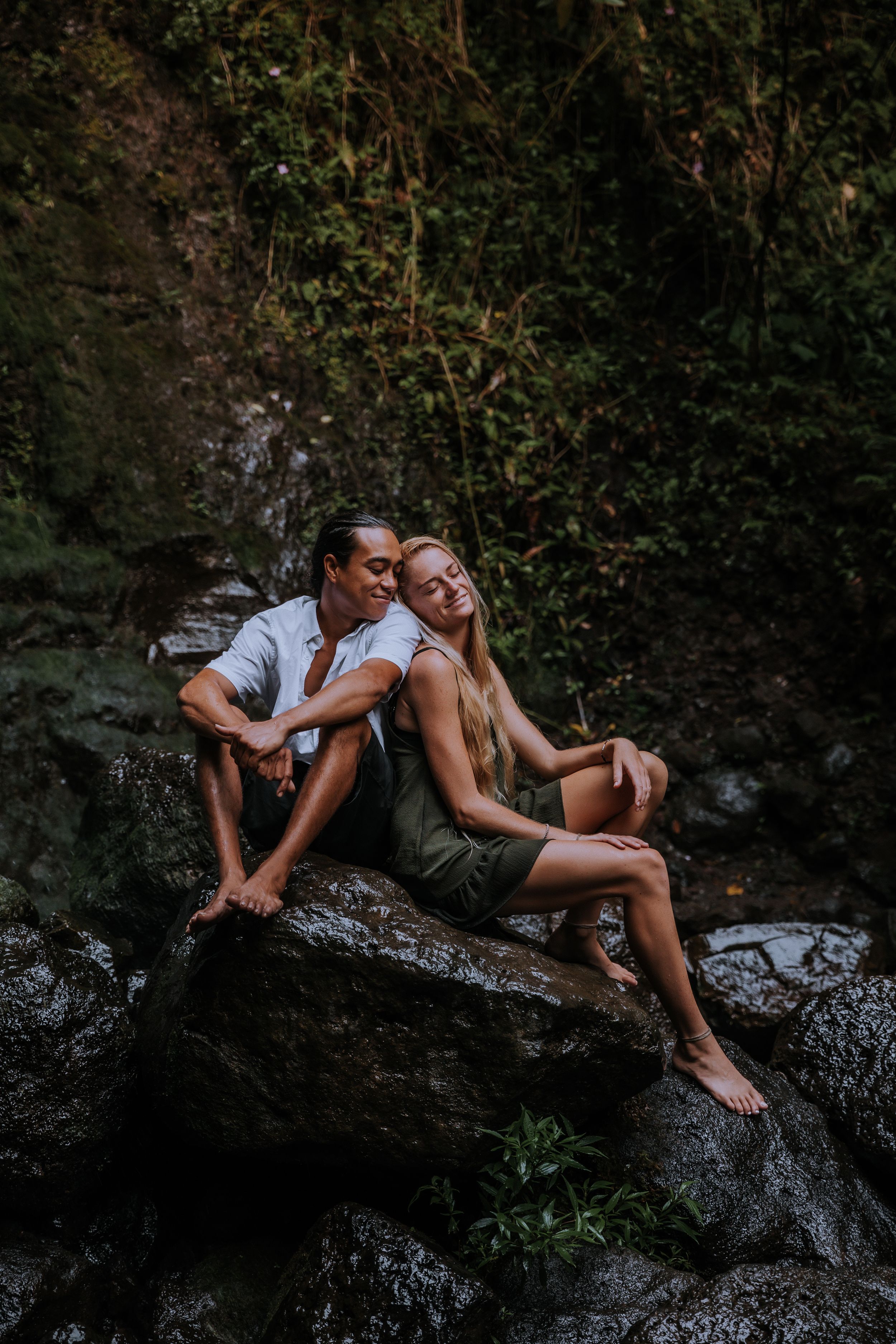 Two people sharing intimate moment on mossy rock formation.
