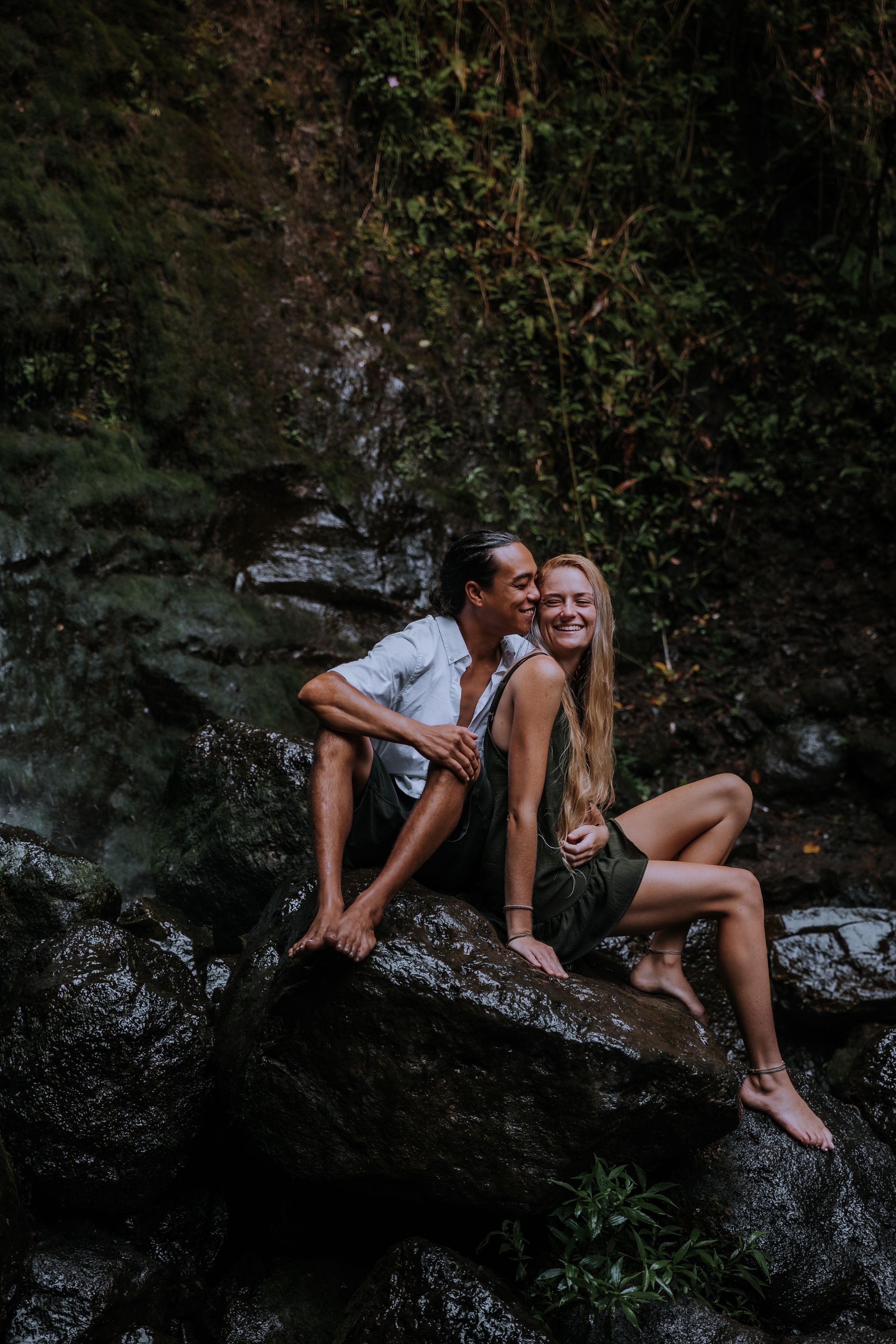Couple sitting together on dark rocky outcrop in natural setting.