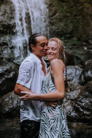 A couple in white clothing embracing near a waterfall.