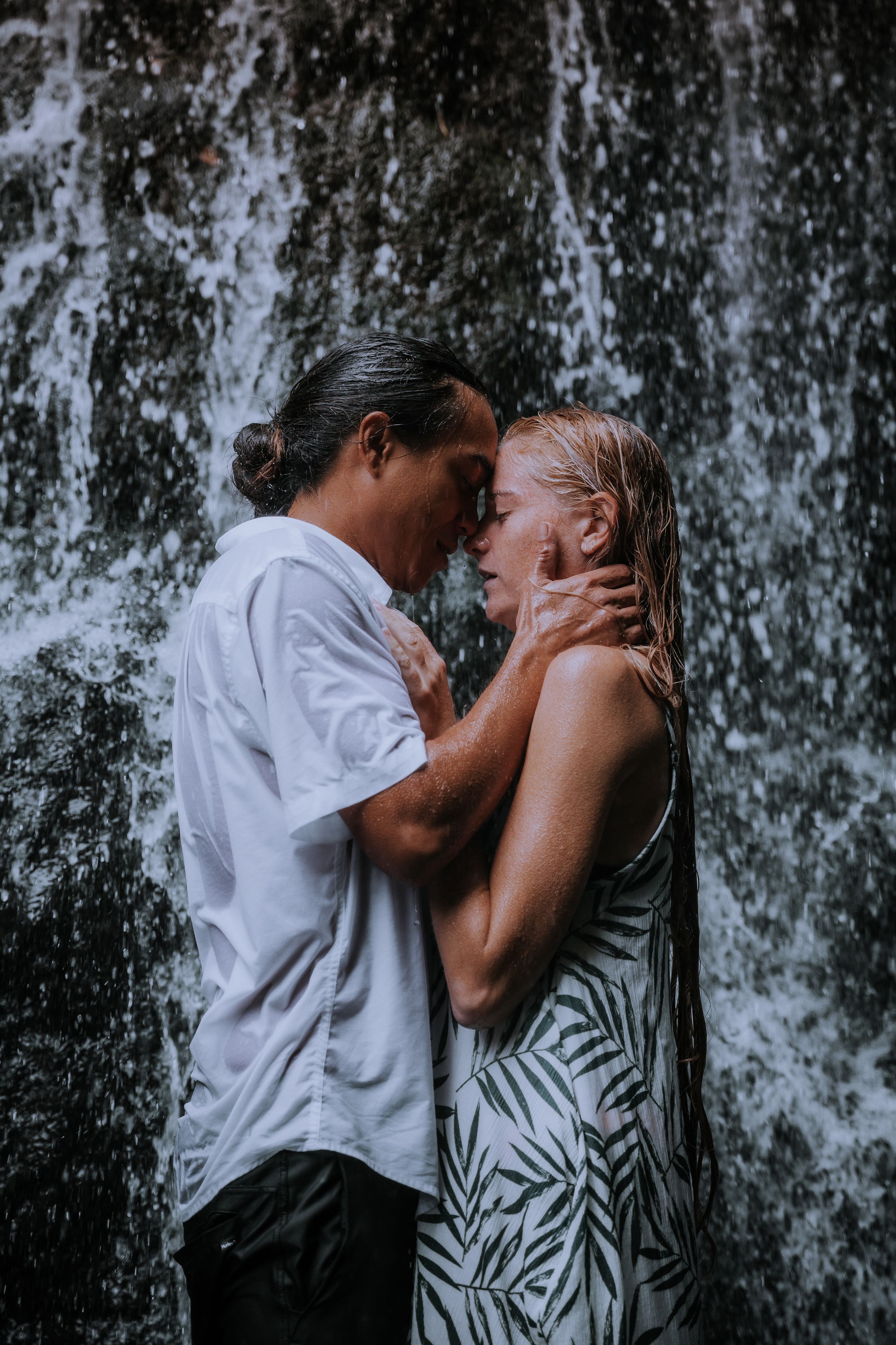 A couple kissing passionately in front of a misty waterfall.