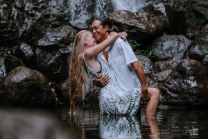 A couple embracing in white clothing against a rocky waterfall backdrop.