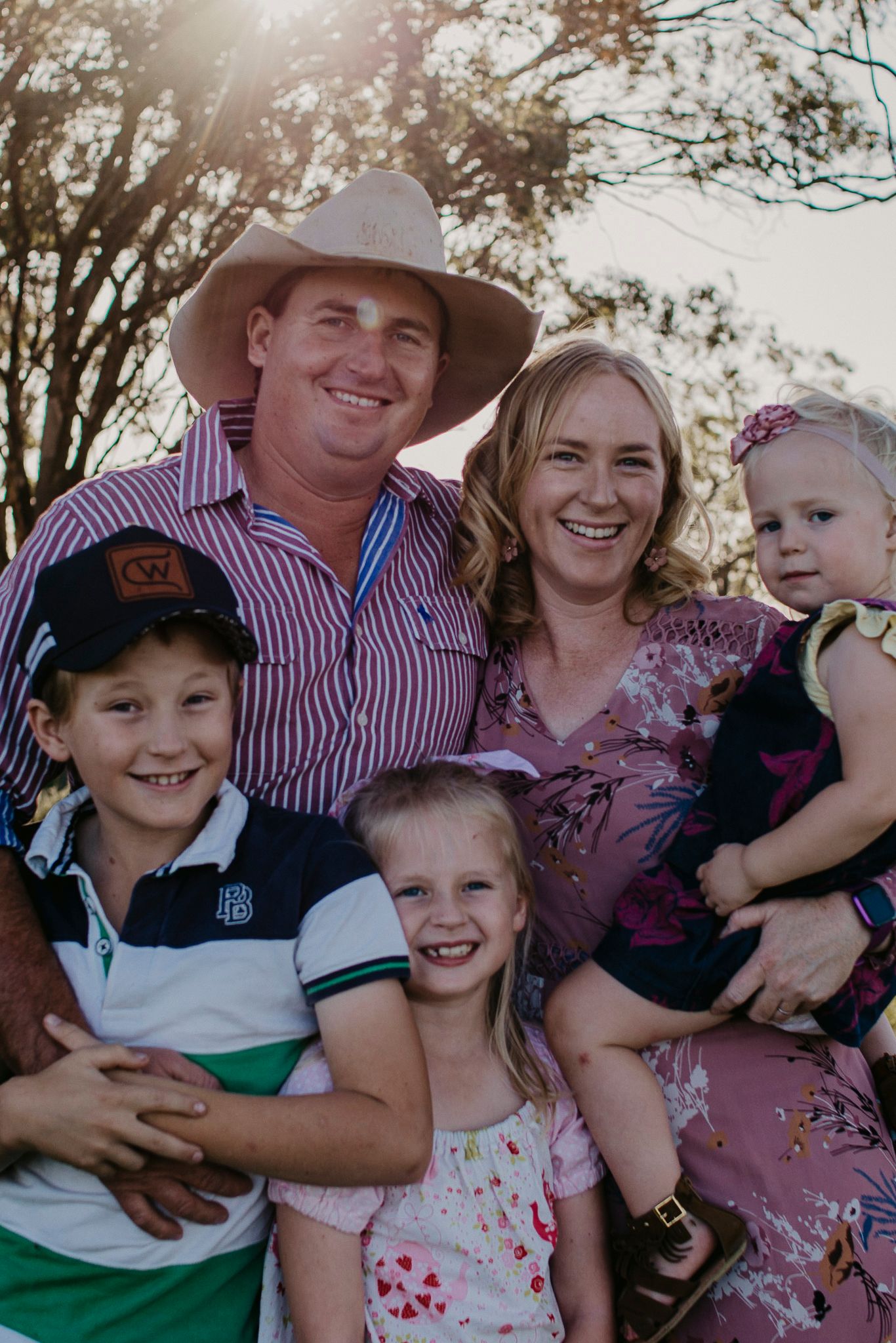Family of five in a rural landscape during golden hour looking at the photographer smiling & relaxed together.