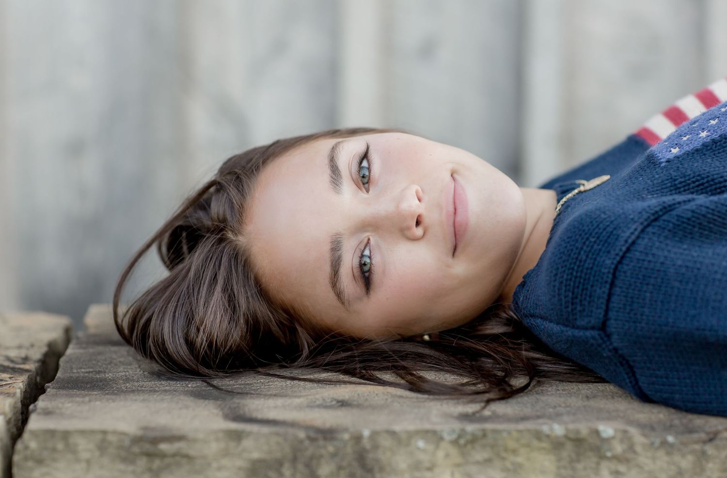 Young woman with brown hair lying on stone surface looking up with a calm expression.