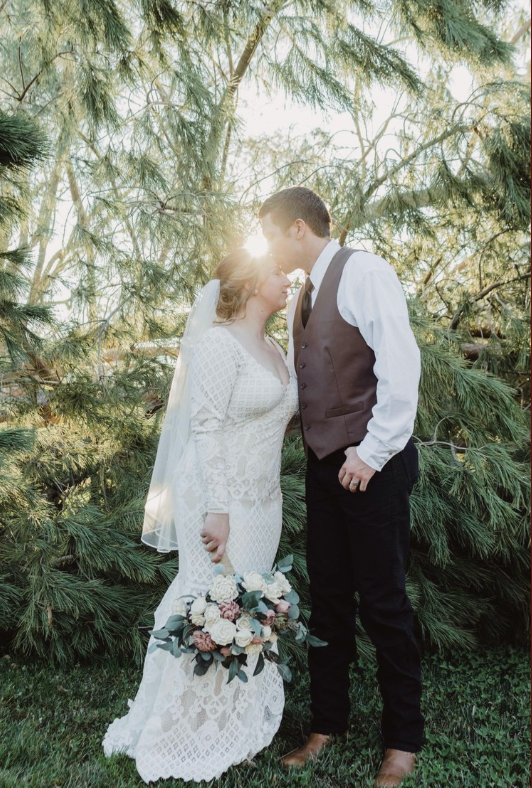 A romantic wedding couple shares tender moments among evergreen trees at sunset in vintage-inspired attire.