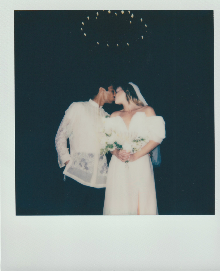 Newlyweds share a romantic kiss under twinkling lights at night.