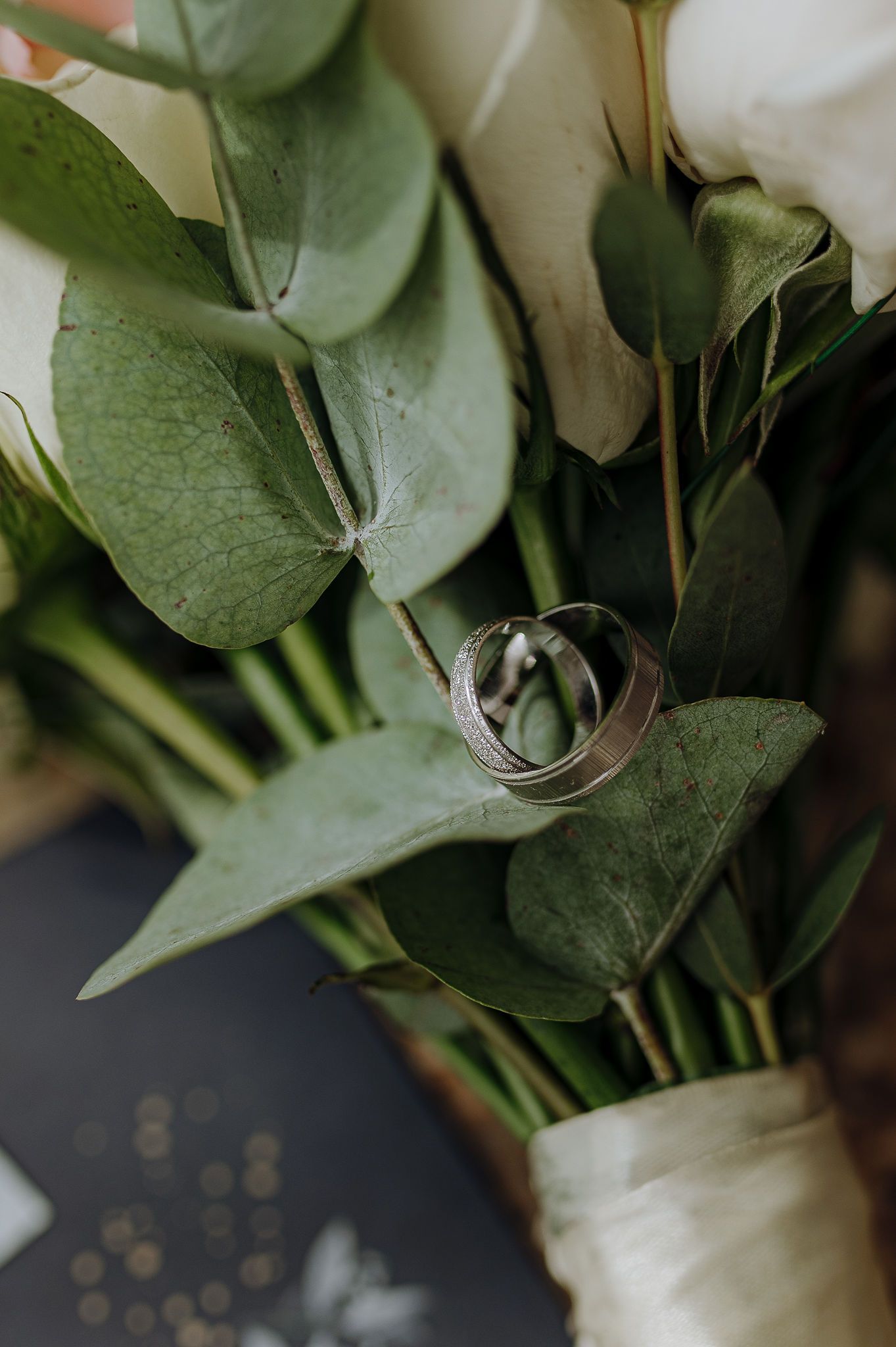 Wedding rings nestled on green eucalyptus leaves in a bridal bouquet.
