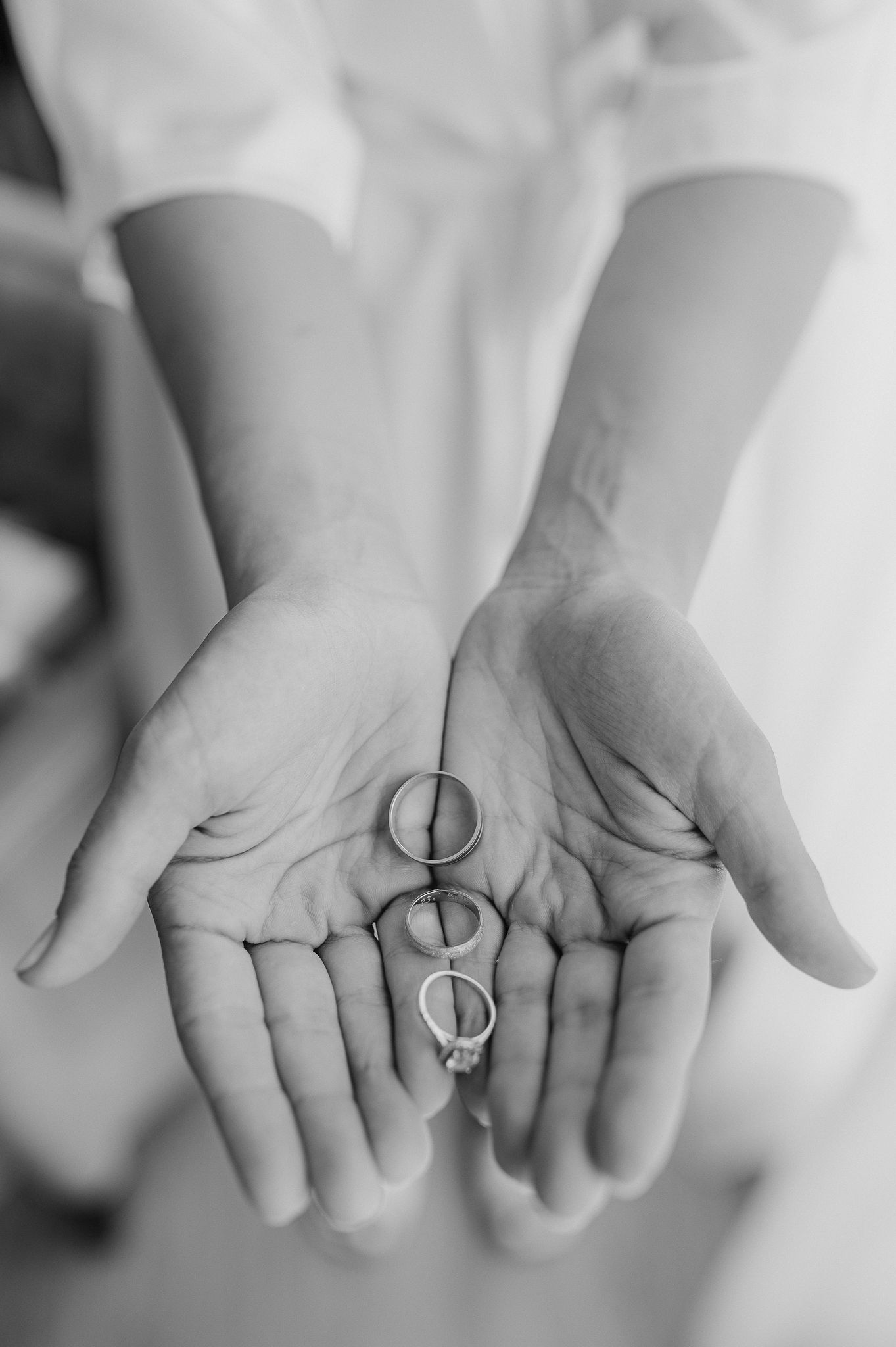 Three wedding rings displayed in open palms, captured in black and white.