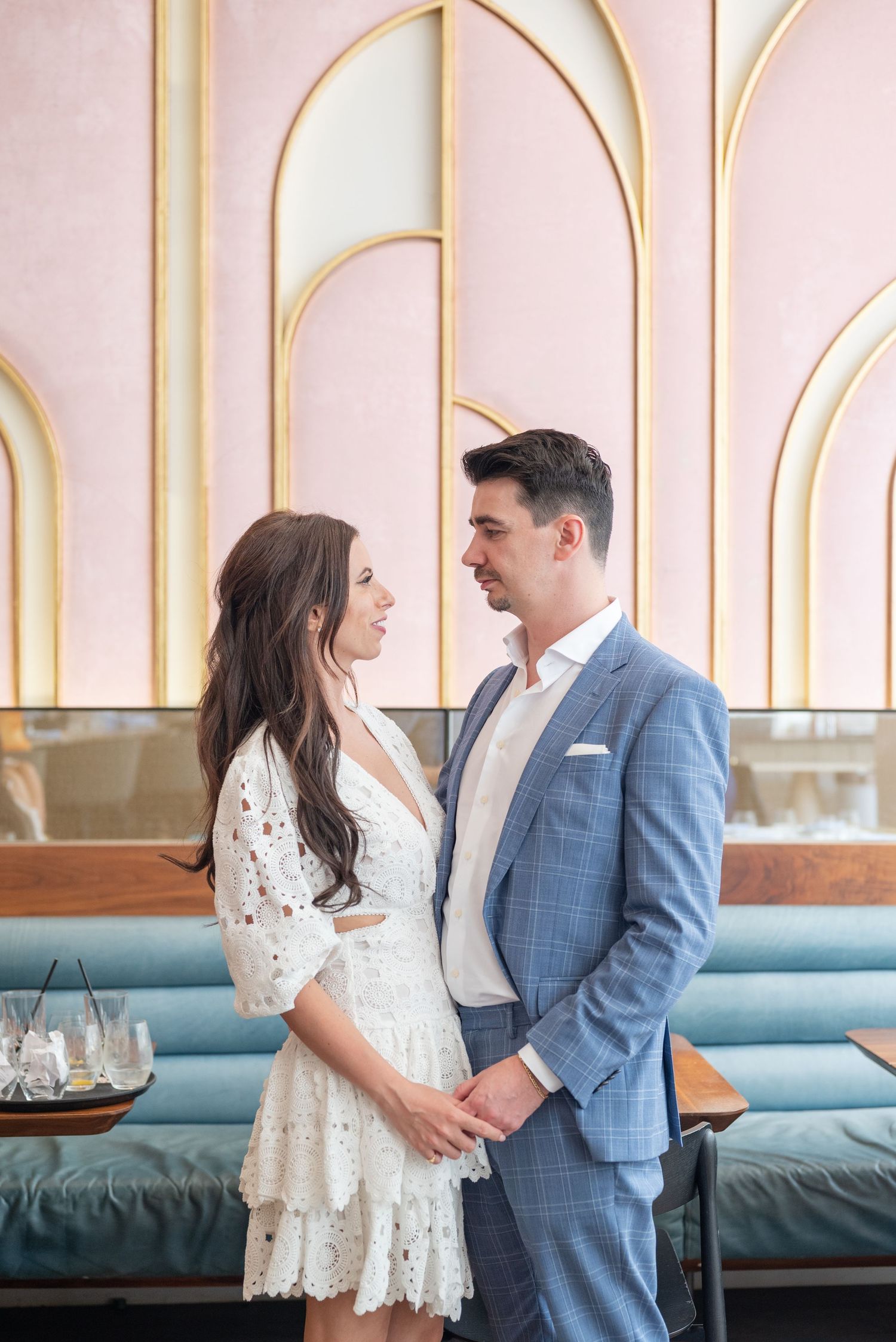 A stylish couple poses in an elegant restaurant with pink and gold art deco walls.