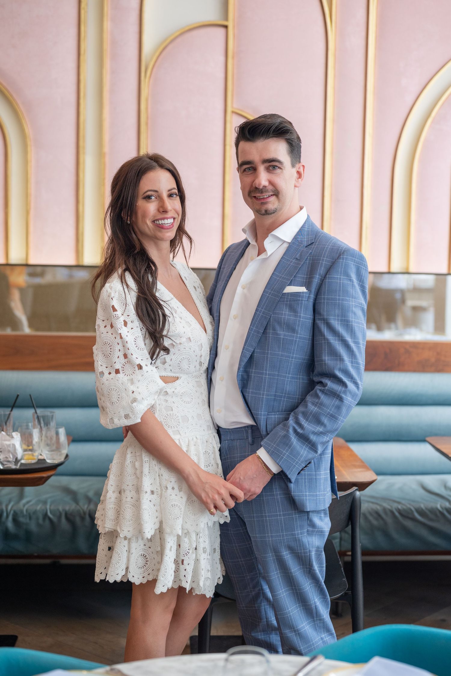 A couple poses together in a restaurant with pink walls and turquoise banquettes.