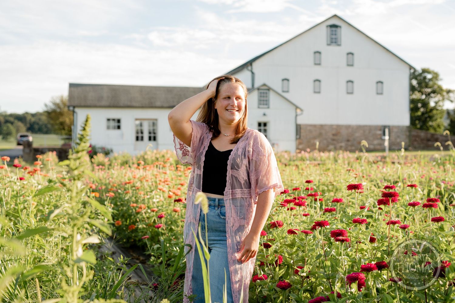 A summer portrait in a wildflower field with red poppies and a white barn in the background.