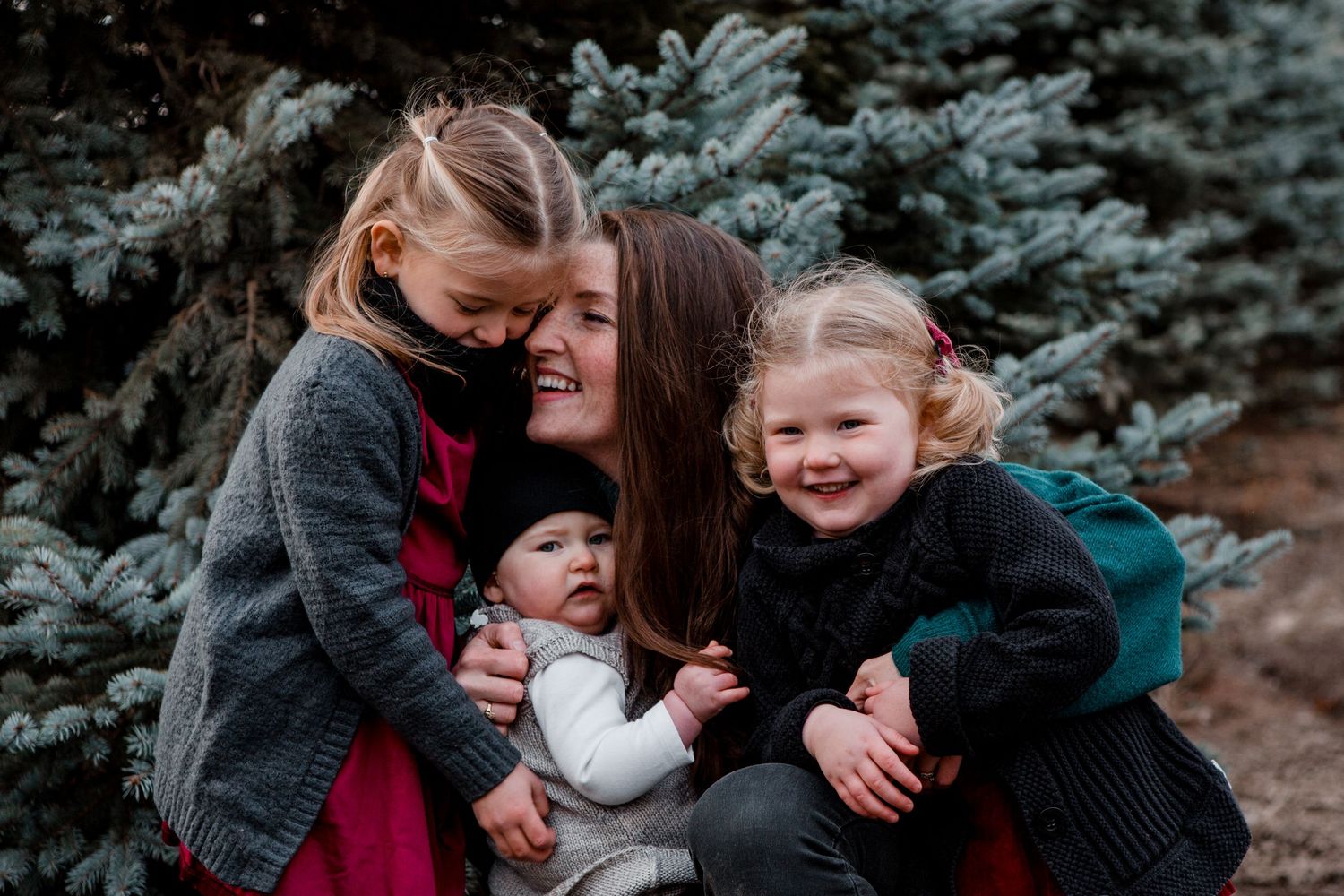 Joyful family moment captured outdoors with evergreen trees in background.