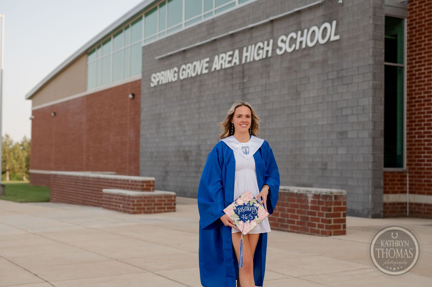 Graduate stands in cap and gown outside Spring Grove Area High School main entrance.