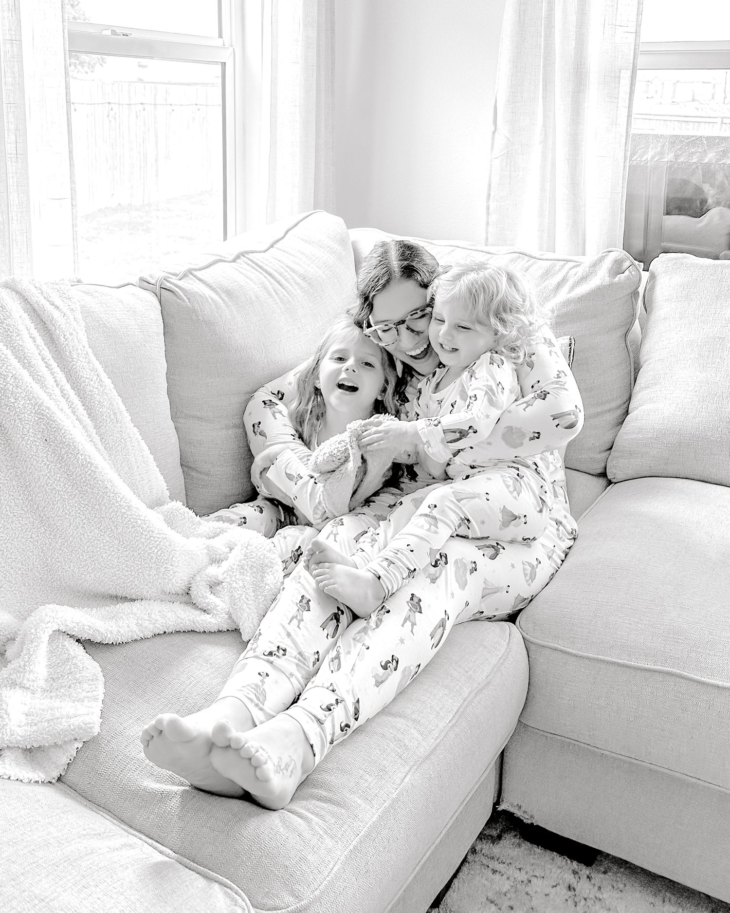 mom cuddling her kids on the couch, as they all laugh together, with matching pajamas on
