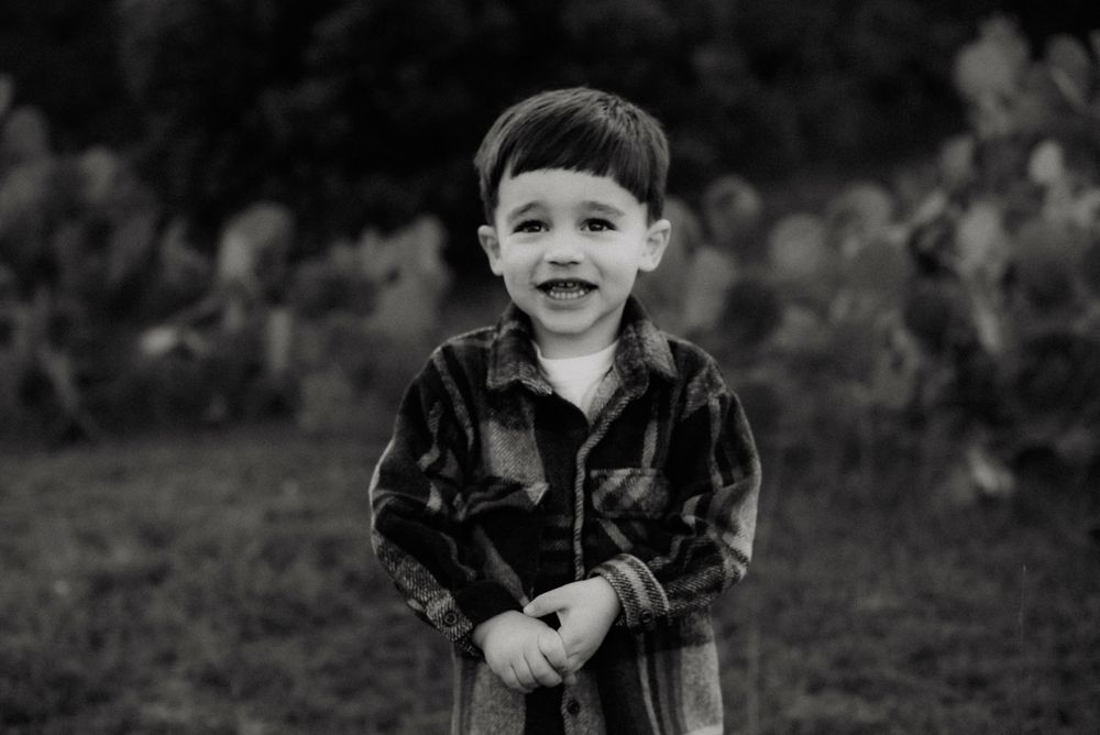 A black and white portrait of a cheerful young child wearing a plaid jacket outdoors.