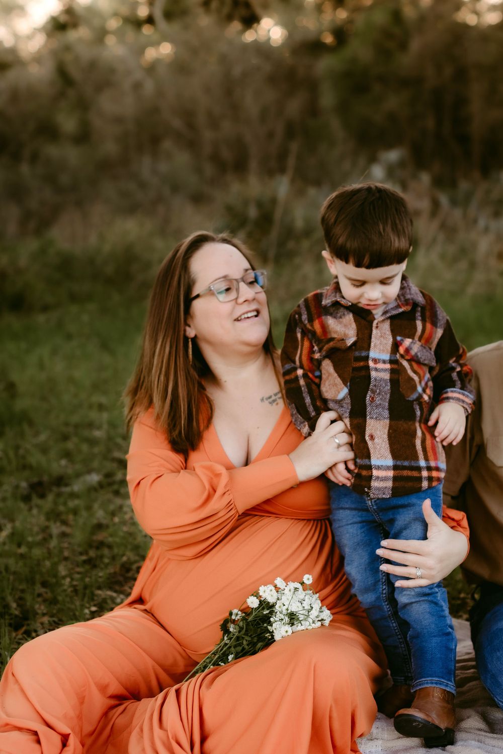 Candid maternity photo showing mother and child sharing a laugh on white blanket outdoors.