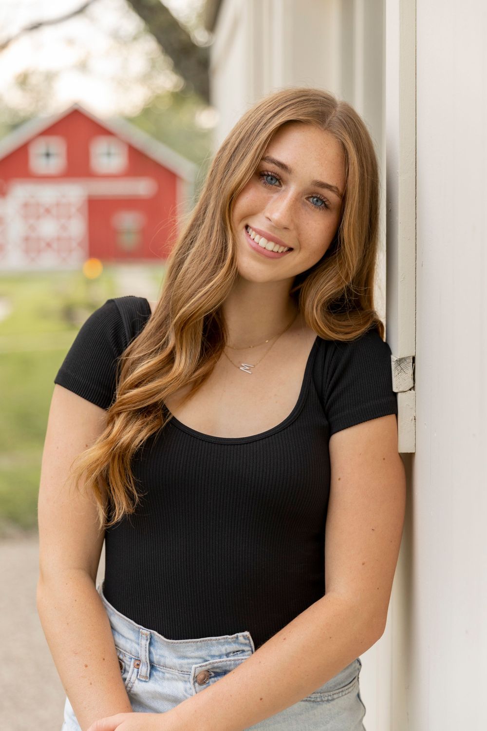 girl leaning against a barn and smiling for senior photos at cranberry lake park